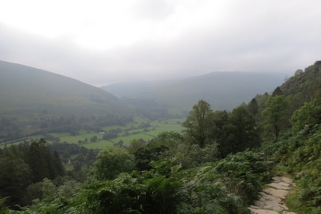 A green valley, the hillsides around it hazy in low cloud and mist.