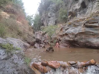 A person bathes in a pool in a river in some kind of canyon.