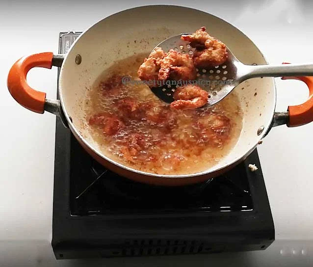 Using a slotted spoon, carefully lift the fried prawns from the hot oil, allowing any excess oil to drain back into the pan.