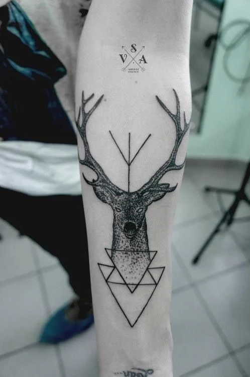 Vemos un antebrazo, con tatuaje de ciervo y de triángulos