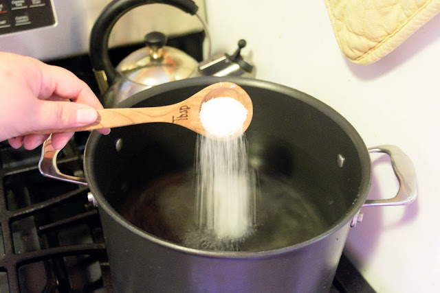 A pot of water on the stove with salt being added to it. 