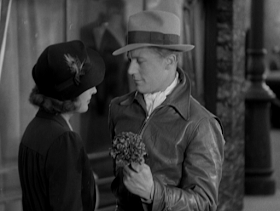 Michael (Gene Raymond) offers Carolyn (Barbara Stanwyck) a small modest bouquet of flowers.