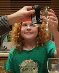 small boy with fancy port glass full of cola chinking glasses in a toast with others off screen