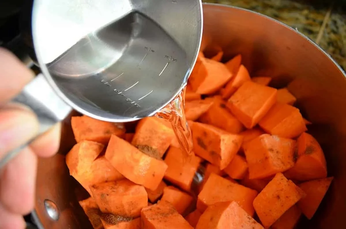 Diced Yams, Salt, and Cinnamon in a stainless steel pot with water being poured in.