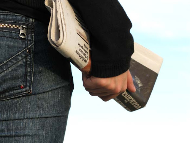 Homem de jeans carregando um jornal na mão.