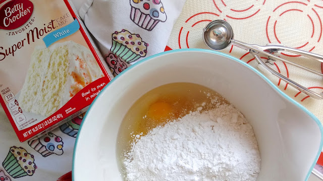 The ingredients for the Victoria Sandwich Whoopie Pies sitting in a bowl next to a baking sheet, cookie scoop, tea towel, and a box of cake mix