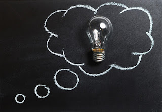 A though bubble is drawn on a chalk board. A lightbulb sits on the chalkboard, placed inside the thought bubble.