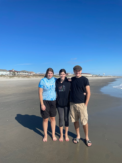 Elizabeth, you, and Andy standing on the beach facing the sun arms around each other. This pic was taken while on our long walk the day we got into town. The ocean is on the right and the shoreline is on the left.