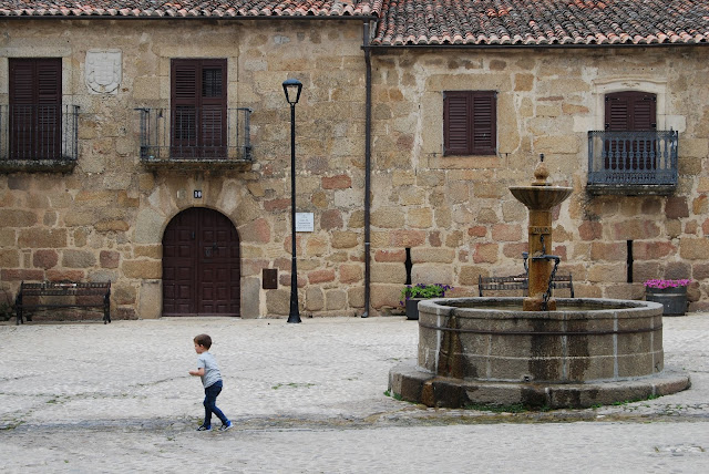 Niño en la plaza de San Martín de Trevejo con sus fachadas de piedra y su fuente circular en el centro