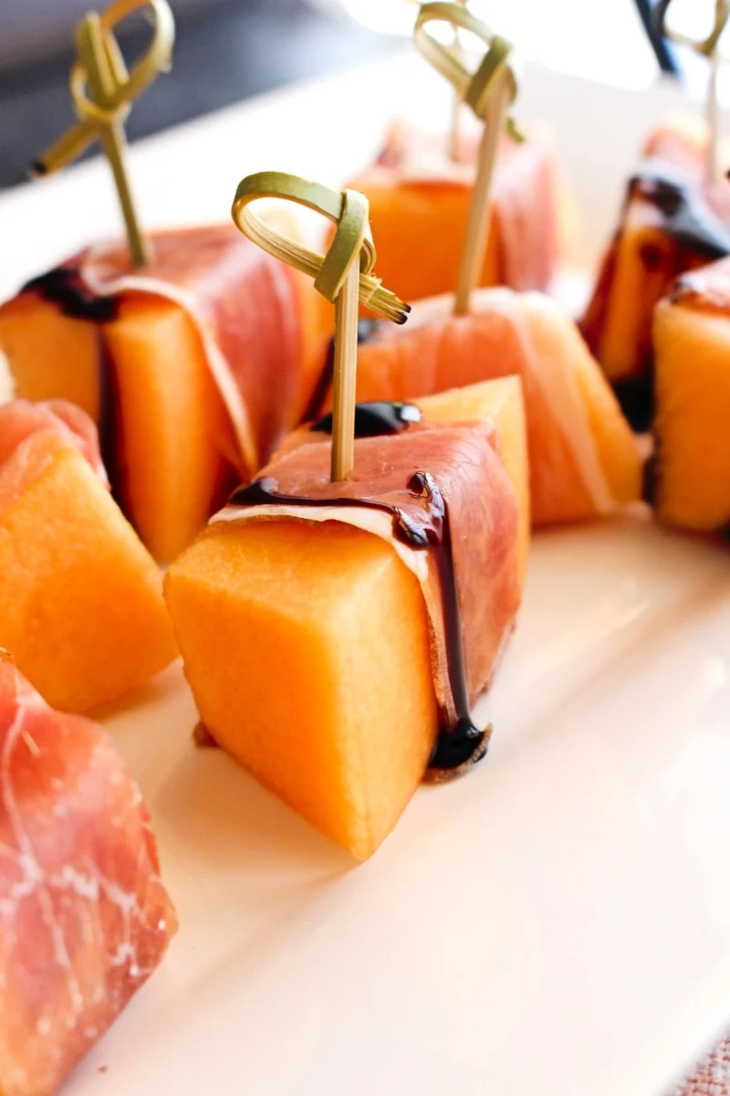 Side view of proscuitto wrapped cantaloupe on a white plate with a pink background