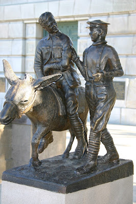 Sculpture of a wounded soldier astride a donkey being led by a medical corpsman