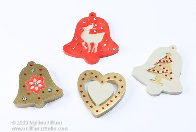 4 gold, white and red handmade Christmas ornament shapes - bell with flower centre, bell with reindeer, heart with inner cutout heart and bell with Christmas tree. Each one is embellished with sparkly red or clear crystals