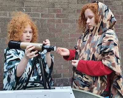 Boy assembling telescope outdoors wearing over the head blankets