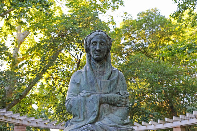 Una estatua de una mujer con copas de árboles al fondo.