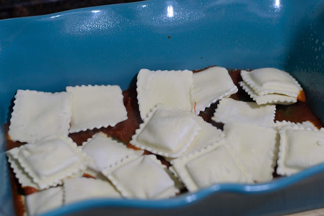 Frozen ravioli being added to the baking dish. 