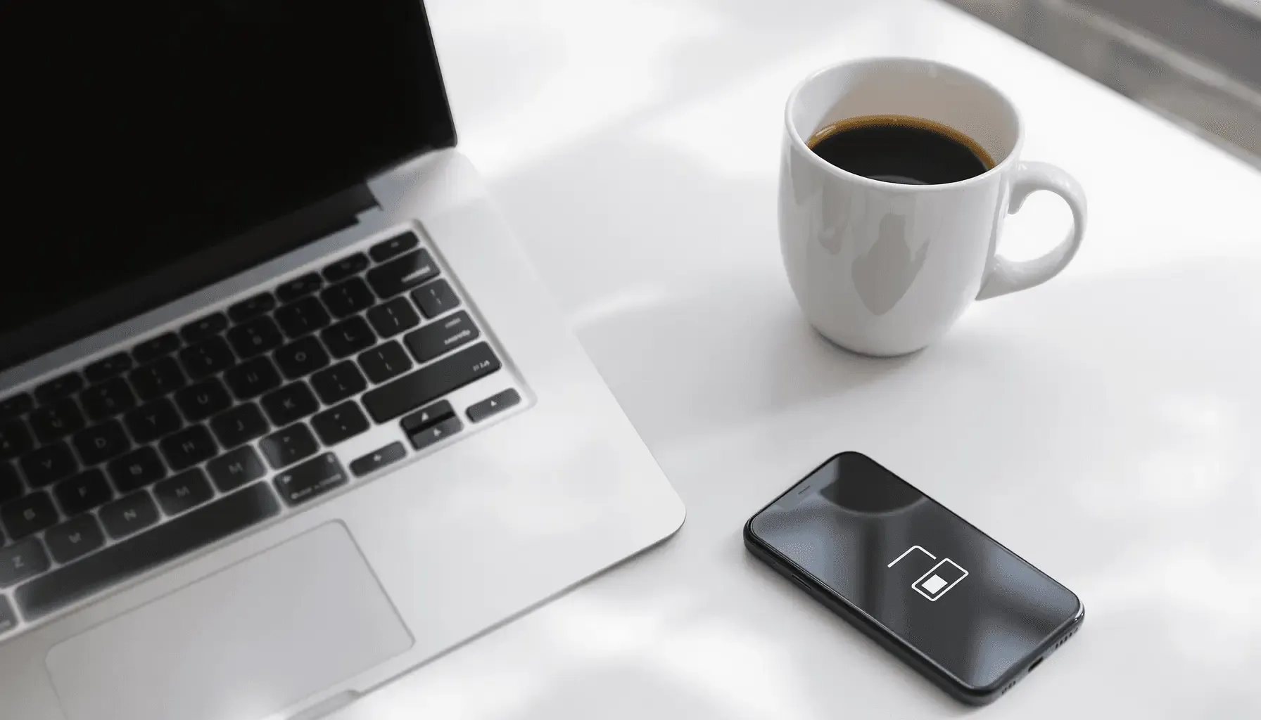 Laptop, coffee mug, and smartphone on a white table.