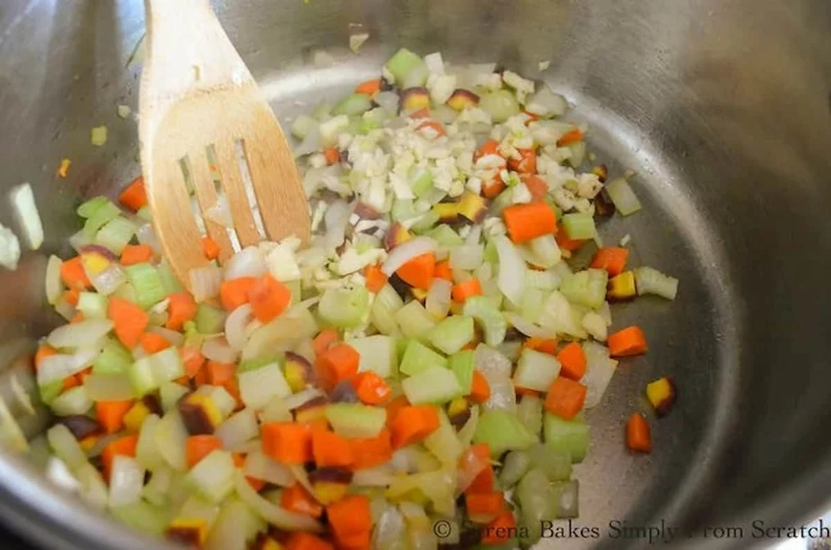 A down shot of onions, carrots, celery, and minced garlic in a large stainless steel soup pot.