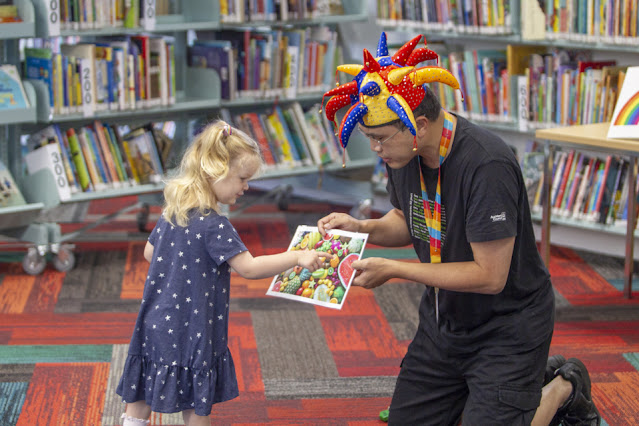 Librarian handing book to small girl in library.