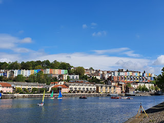 Photo of Bristol harbour in the sun with sailing boats on the water and colourful houses overlooking