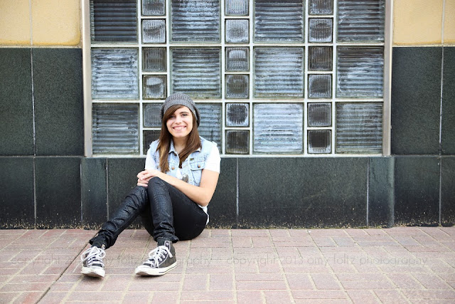 photo of a teen girl sitting on a sidewalk in front of a glass brick wall