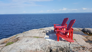 A pair of Parks Canada red Muskoka chairs on a rocky outcrop at Les Escoumins, north of Tadoussac, QC.