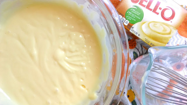 a bowl of banana cream pudding next to a measuring cup and box of pudding mix