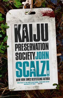 Ebook cover of The Kaiju Preservation Society (a plastic blood-stained lanyard sitting on a dense jungle floor bears this novel’s title)