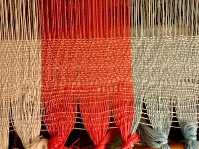 close up of the start of a woven project on a floor loom, showing the header and first few inches of weaving. The header has been woven with the weft thread and there are 6 picks, spread about half an inch apart. After the header is two repeats of diamond twill weave, over about three inches. The diamonds are very elongated from the loose beat and there is a lot of space between the warp and weft threads.