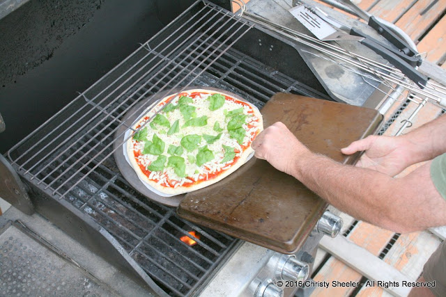 Pizza is positioned in center of pizza stone on grill.