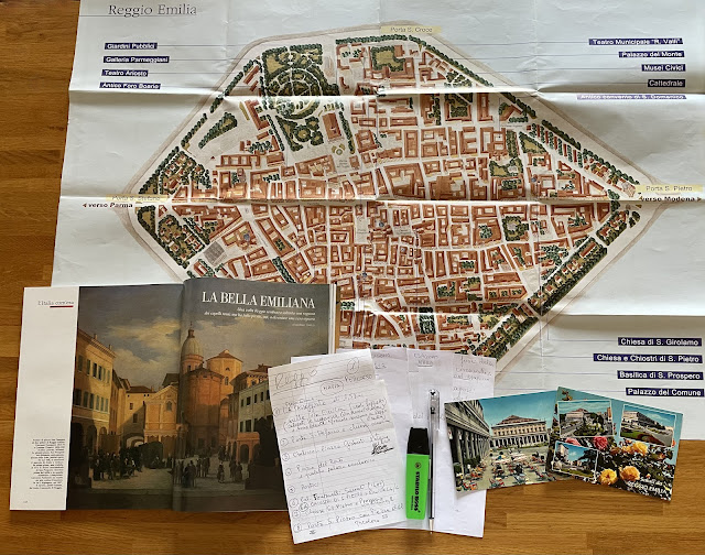 Cartina del centro storico di Reggio Emilia, insieme a una rivista aperta, cartoline, appunti scritti a mano, biro e pennarello.