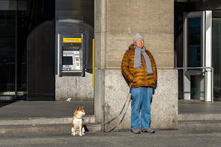 Ein Mann geniesst die wärmenden Sonnenstrahlen, während er mit seinem Hund vor der Post wartet.