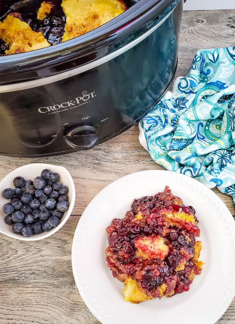 cake on a white plate next to a black slow cooker.