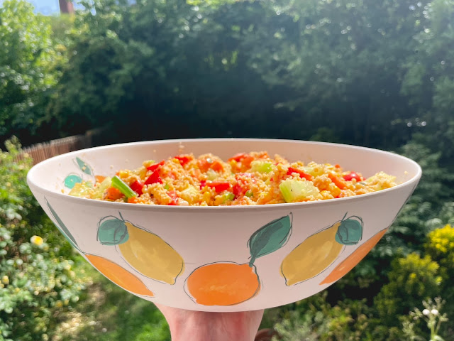a large bowl of cous cous salad being held up against a background of a very green garden