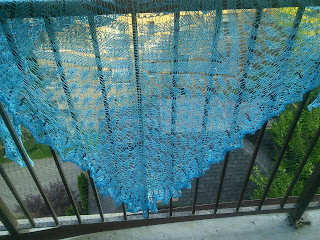 A lace, light-weight blue shawl hanging over a fence.  There are black circular beads in the edging. 