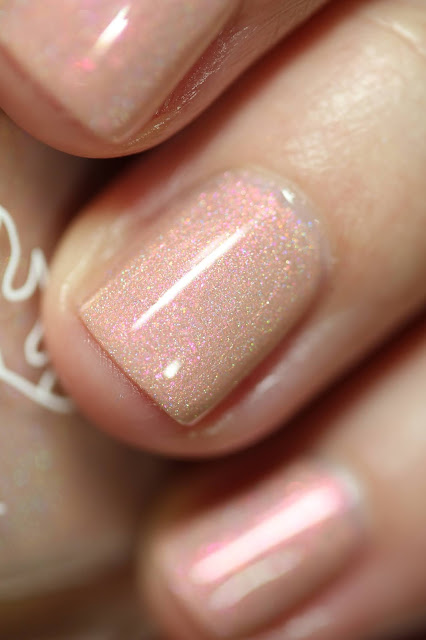 peachy holographic nail polish with red shimmer swatched on white person's nails