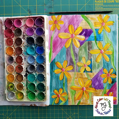 A floral coloring page is brightly painted in happy colors. A well loved palette of watercolors lies next to it.