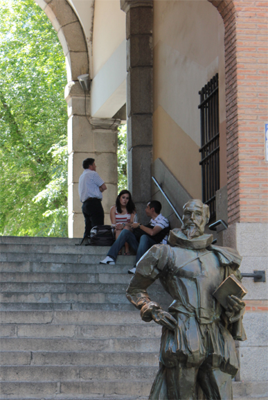 zwiedzając starówkę Toledo przy schodach w kierunku Plaza de Zocodover. Na pierwszym planie rzeźba Cervantesa - brodatego meżczyzny,  w renesansowym stroku, z książką w dłoni. W tle schody ku placowi. Na schodach siedzą rozmawiając dziewczyna i chłopak.