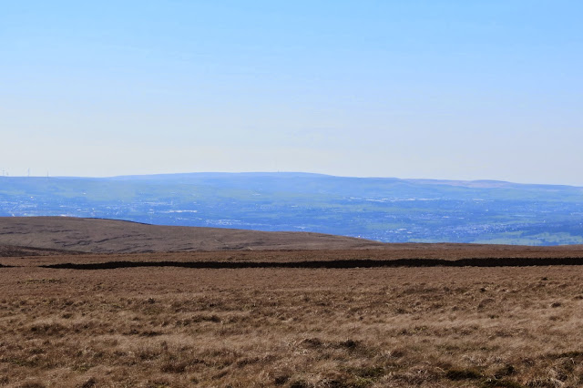 A view across the expanse of Pendle Hill to the broad outline of Winter Hill on the horizon, with its TV transmitter just visible in the haze.