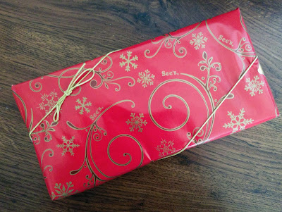 A box of See's Candy wrapped in red Christmas wrapping.