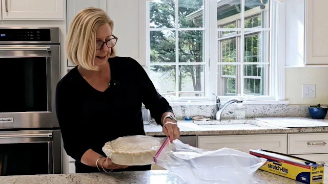 A woman placing an apple pie into a large freezer bag.