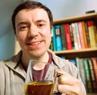 Martyn Greenwood holding mug of tea in front of a bookcase