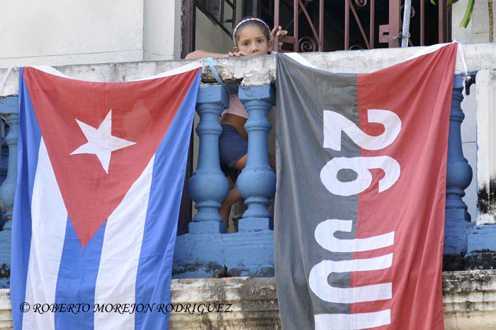 Una niña mira desde un balcón engalanado con una bandera cubana y otra del Movimiento 26 de Julio, en La Habana, Cuba, el 24 de julio de 2013.