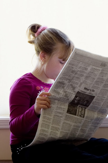 A youg girl reading a newspaper.