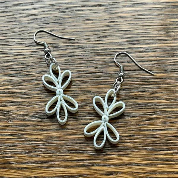 pair of ivory paper quilled earrings with silver ear wires displayed on wooden table