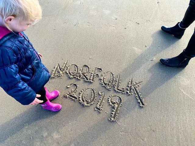  a child looking at writing in the sand saying Norfolk 2019 which seemed appropriate for a weekend away