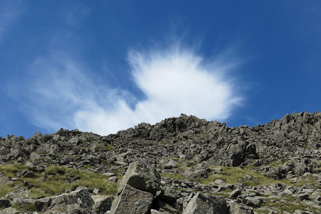 A bright cloud feathering out in the sky above a rocky ridge.