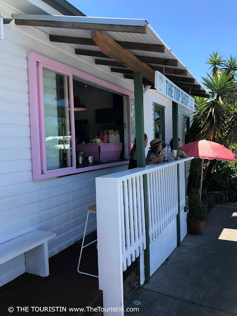 People drinking coffee on the verandah of a white weatherboard house with pink window frames.