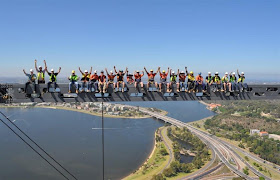 A bunch of construction workers standing on the steel beam high in the air on top of the skyscraper