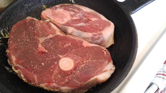 Two lamb leg steaks resting in a black cast iron skillet.