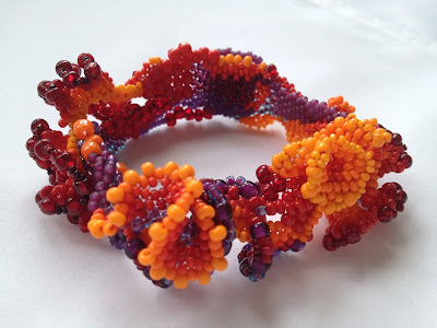 Freeform peyote bracelet shading from yellow-orange to violet through the warm side of the color wheel